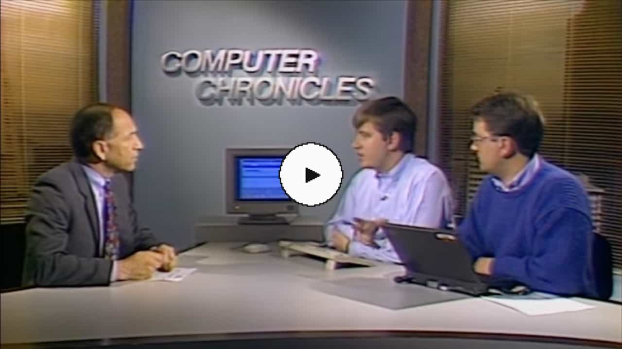 A photograph of two men in collared shirts, both using computers, speaking to another man in a suit. There's a computer in the background and a large title that says 'Computer Chronicles'.