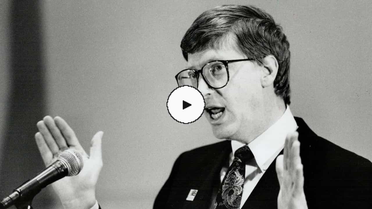 A photograph of Bill Gates speaking with his hand raised. It has a play button on top of it.